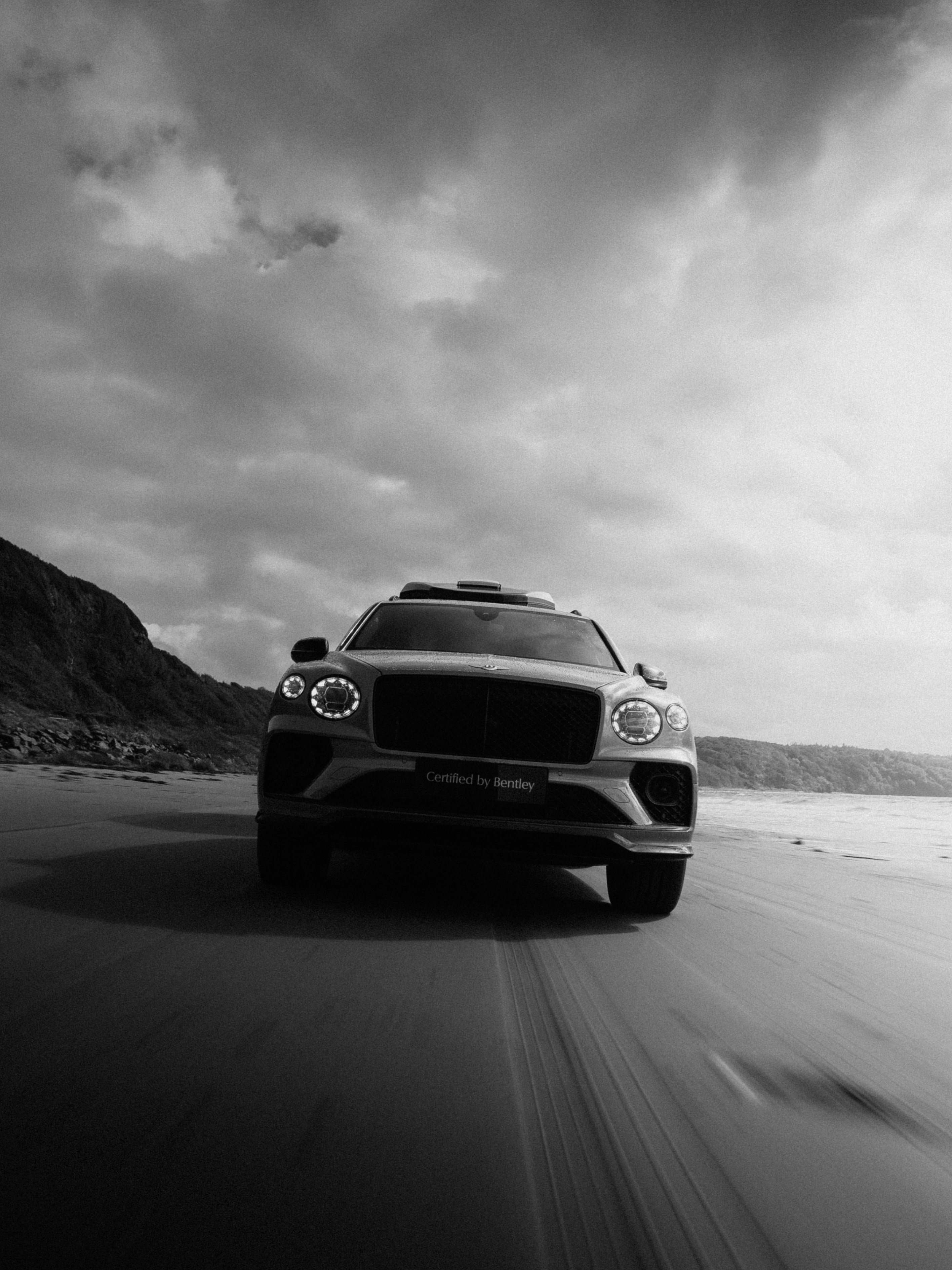 Black and white photo of a Bentley driving along a beach